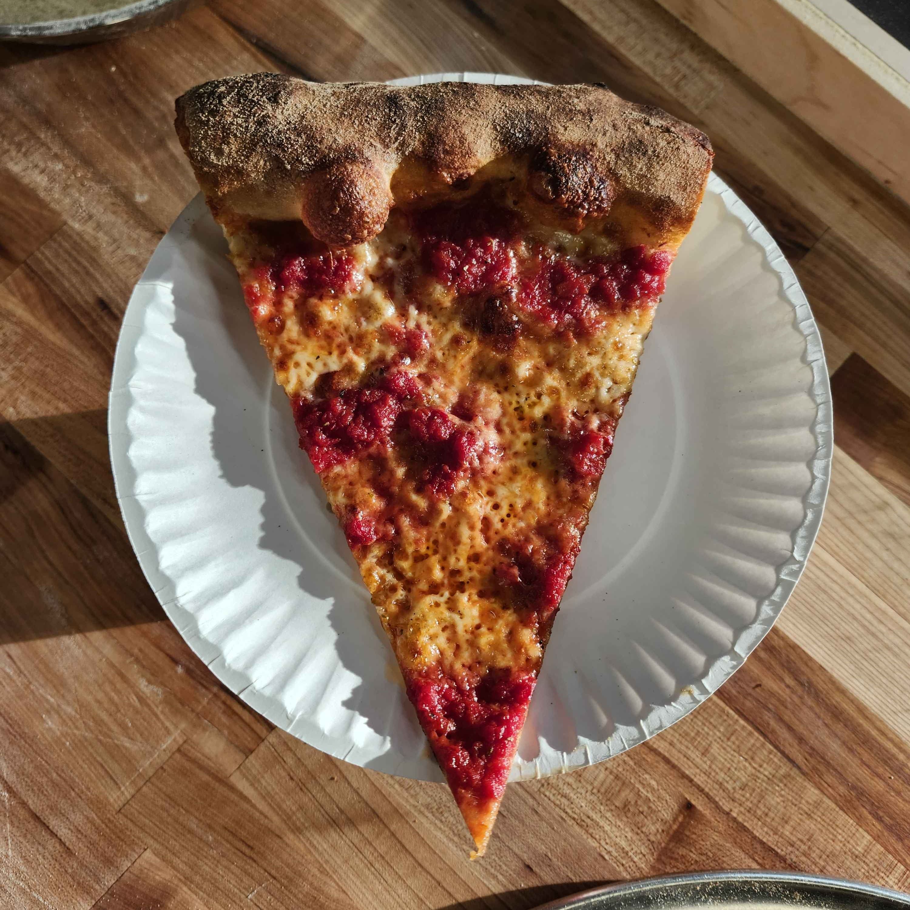 Thin crust cheese pizza slice with tomato spots on a paper plate inside Chomp Pizza in Pilsen Chicago.